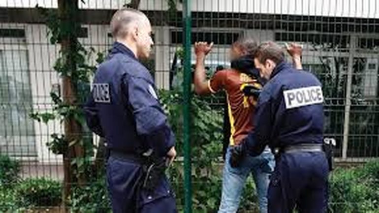 Deux policiers procèdent à un contrôle d’identité sur la voie publique, un citoyen présente ses papiers pendant qu’un autre observe calmement la scène.