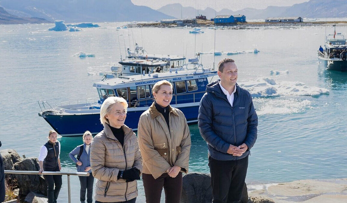 Responsables européens en visite au Groenland avec des navires visibles en arrière-plan.
