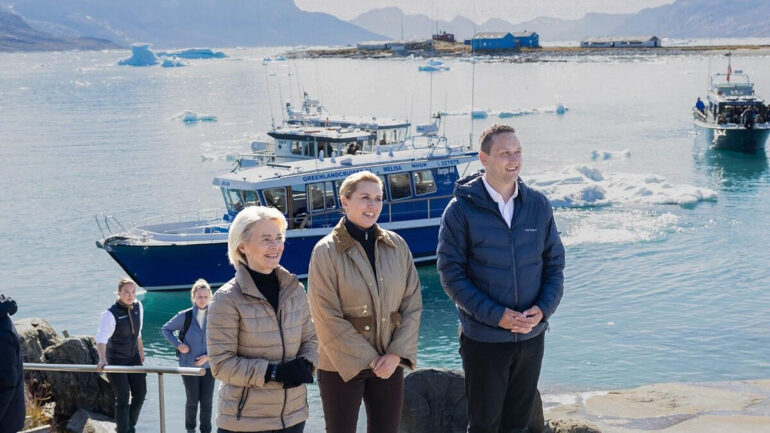 Responsables européens en visite au Groenland avec des navires visibles en arrière-plan.